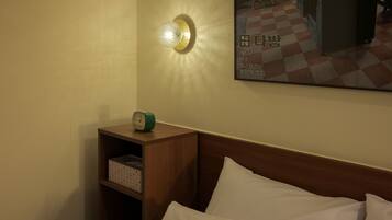 Een hotelkamer met een houten hoofdeinde, een bed met witte lakens, een nachtkastje met een groene wekker en een wandlamp.