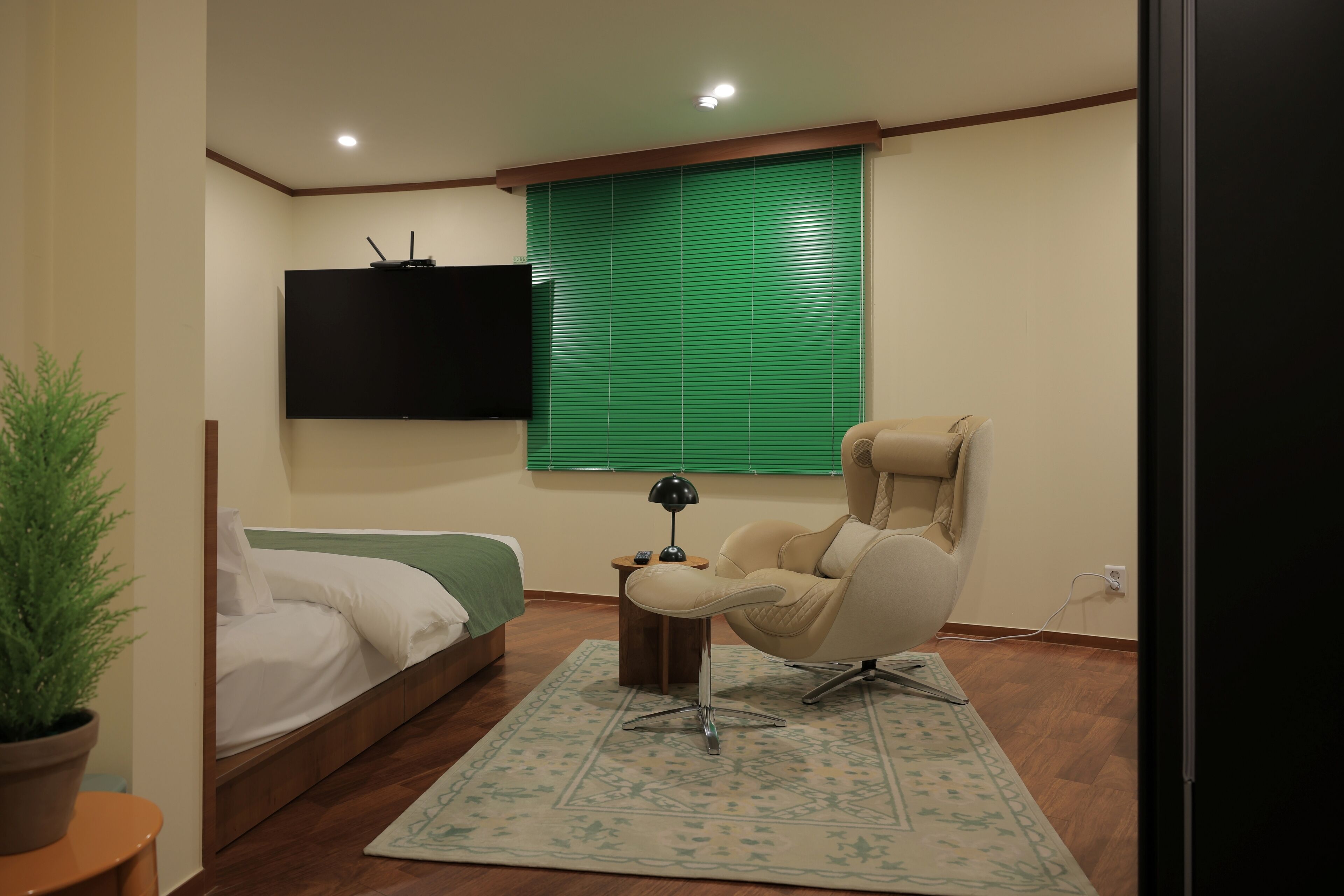 Quarto com cama, cadeira, televisão e janela com persianas.
