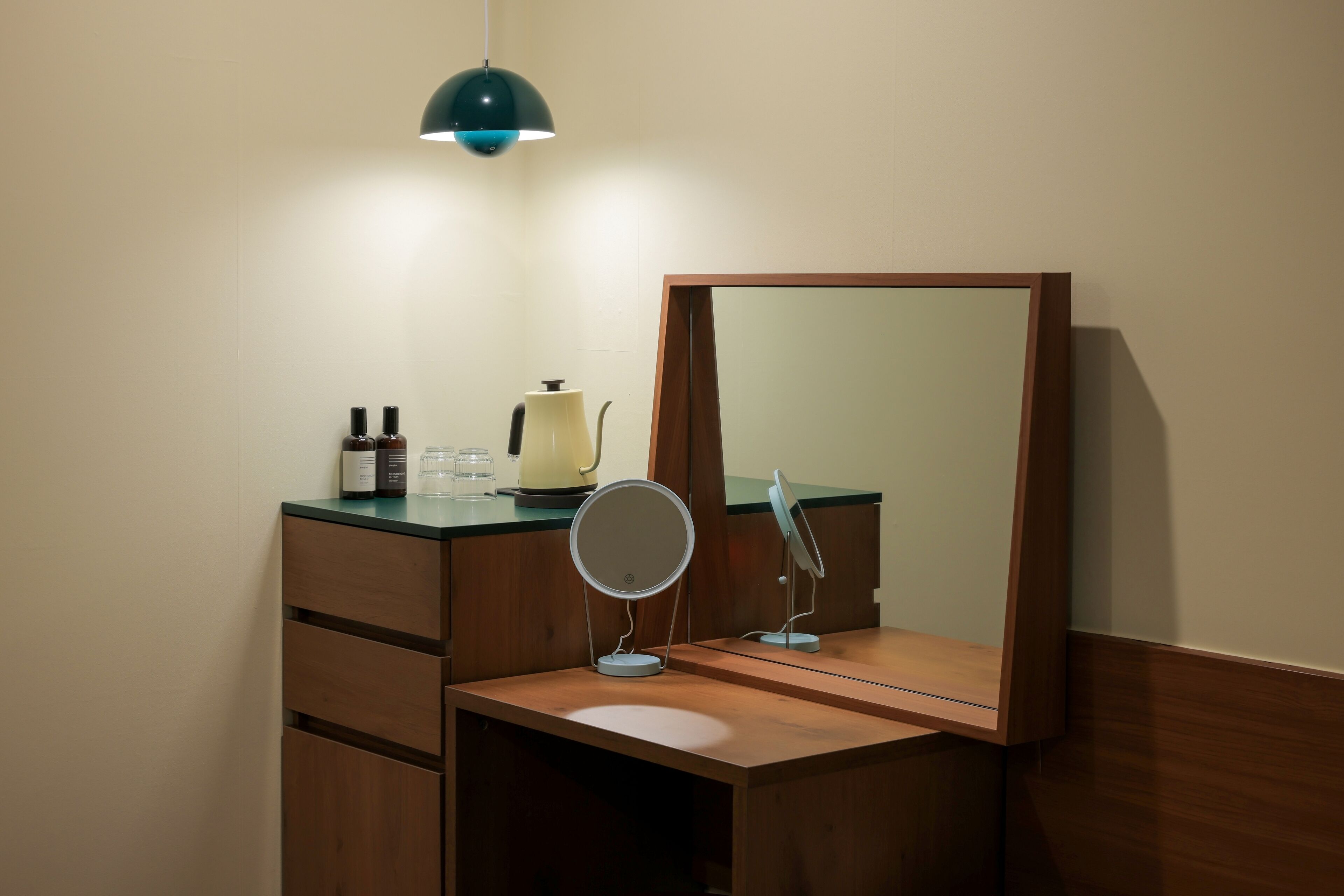 Un baño con tocador de madera, espejo redondo, lámpara colgante verde y artículos de aseo en la encimera.