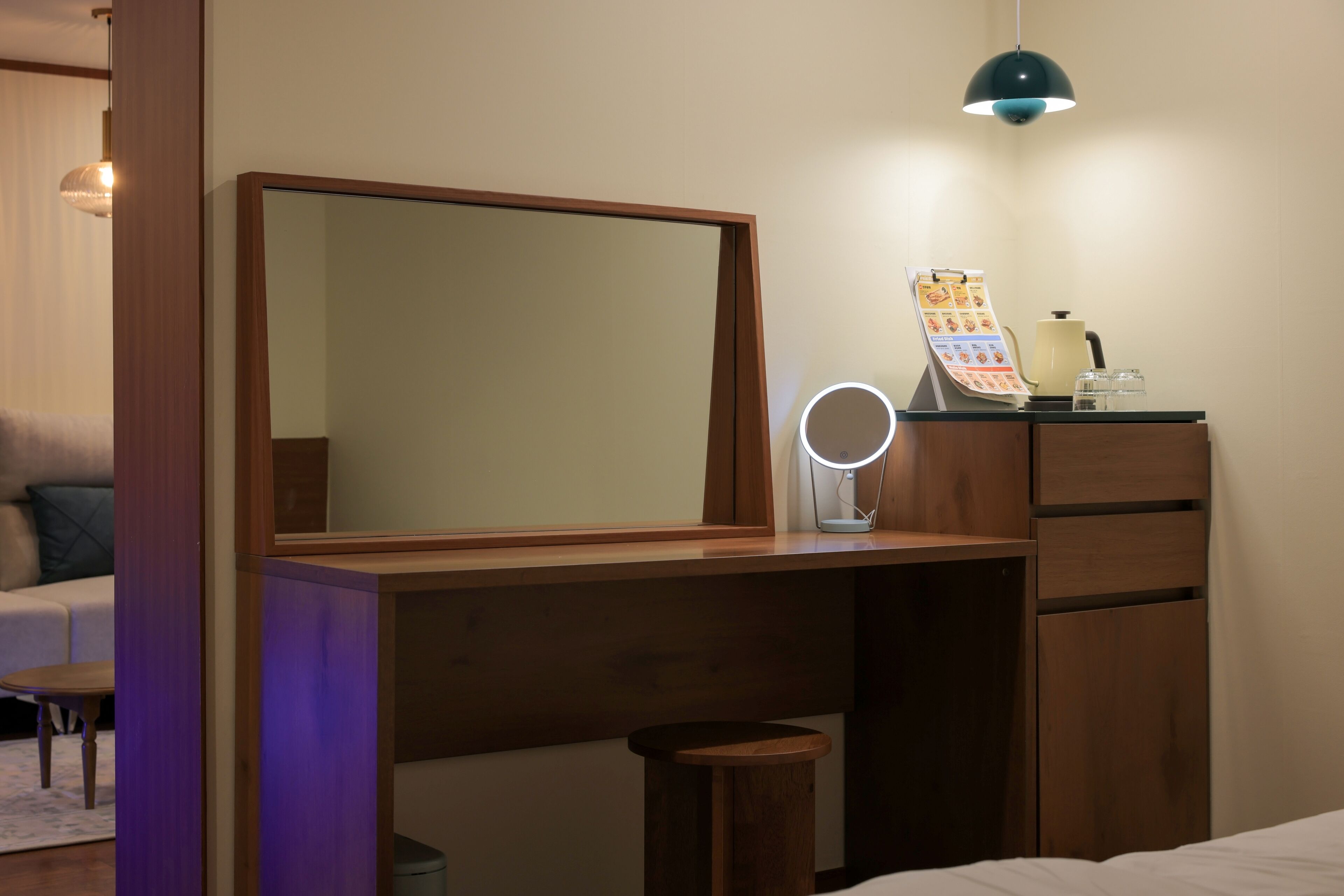 A bedroom with a wooden dresser, a mirror, a vanity with a lamp, and a bed.