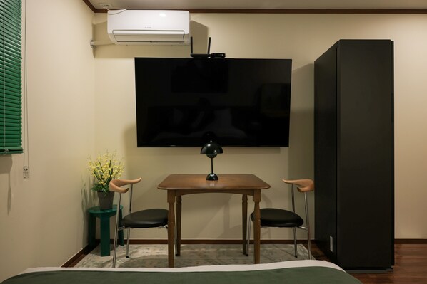 Une petite pièce comprenant un lit, un téléviseur fixé au mur, un réfrigérateur et une table avec deux chaises.
