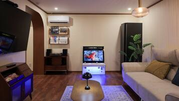 A living room with a flat-screen TV, a Game Box, a sofa, a coffee table, a lamp, and a potted plant.