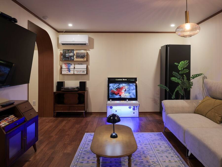 A living room with a flat-screen TV, a Game Box, a sofa, a coffee table, a lamp, and a potted plant.