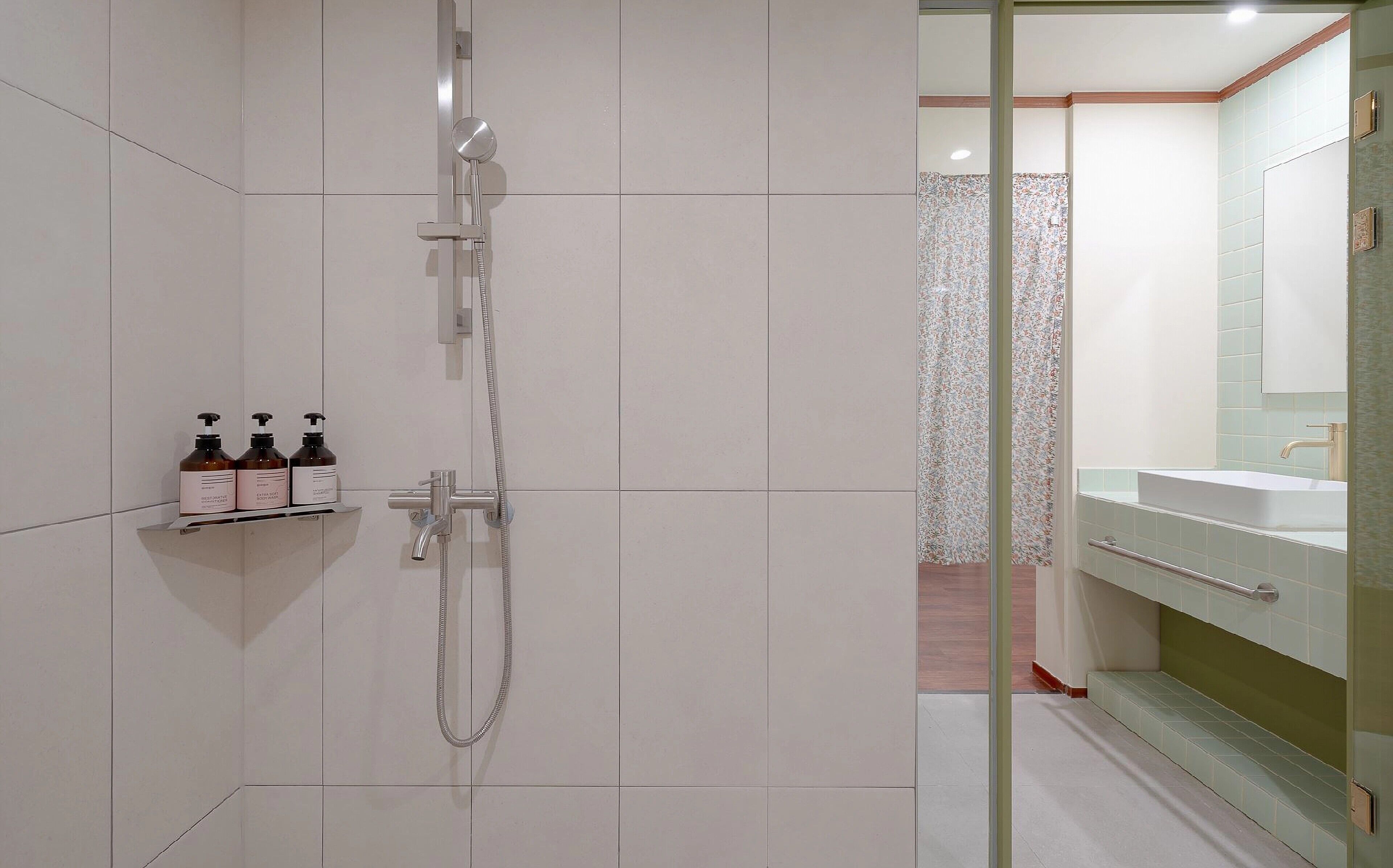 A modern bathroom with a shower, a vanity with a mirror, and two bottles of shampoo on a shelf.