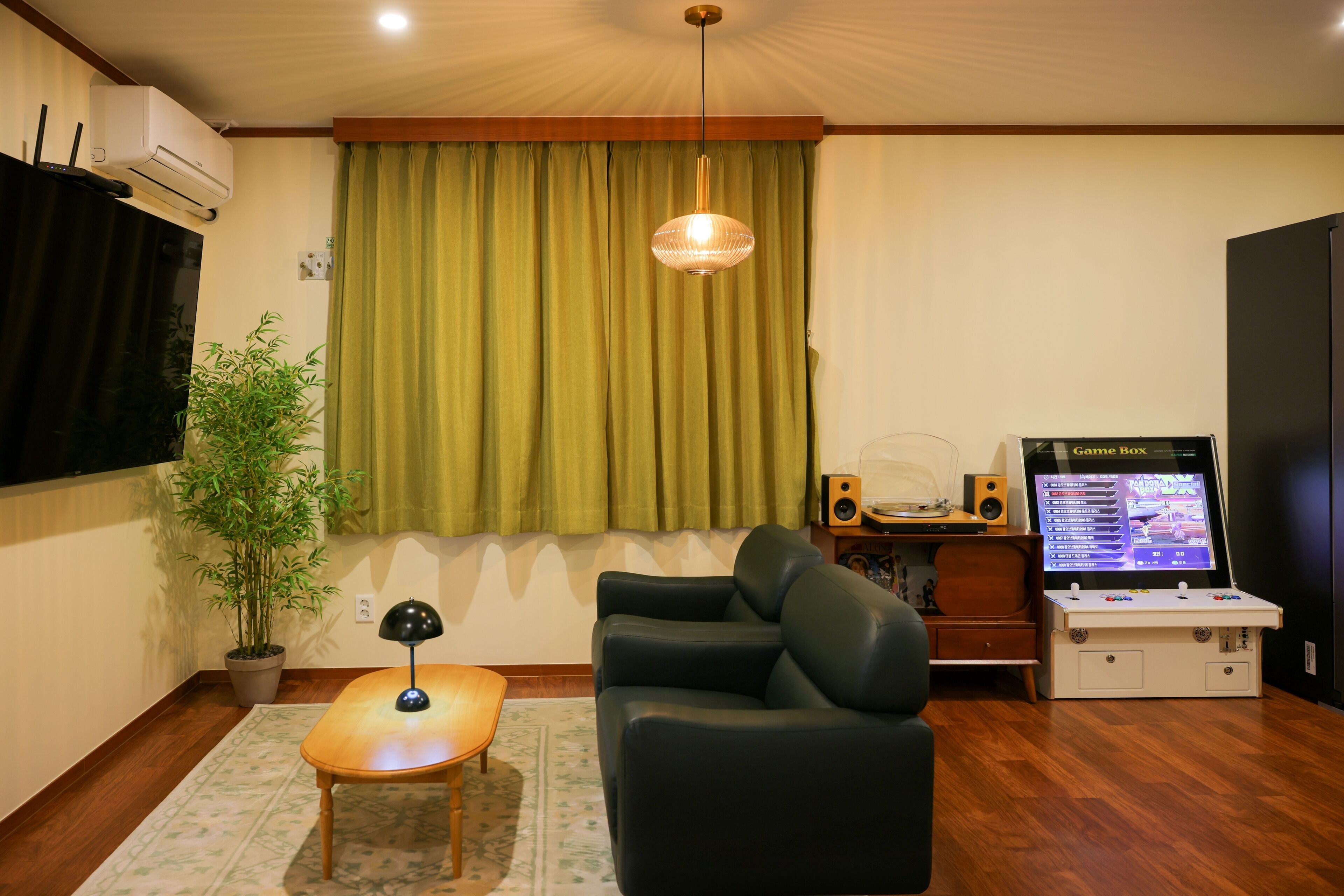 A living room with a sofa, a small table, a potted plant, a hanging light fixture, a television, and a game console.