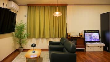 A living room with a sofa, a small table, a potted plant, a hanging light fixture, a television, and a game console.