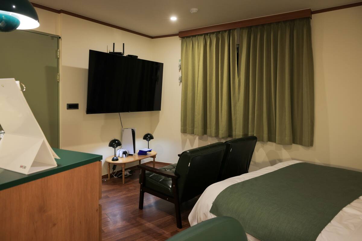 Une chambre d’hôtel avec un lit, un bureau avec un ordinateur, une chaise, un téléviseur fixé au mur et une fenêtre avec des rideaux.