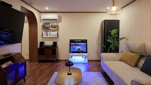 Un salon équipé d’un téléviseur à écran plat, d’une console de jeux GameBox, d’un canapé, d’une table basse, d’un meuble pour téléviseur et d’un climatiseur fixé au mur.