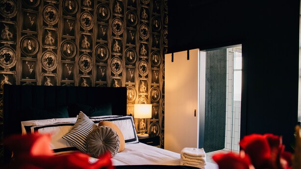 A hotel room with a bed, a nightstand, a lamp, and a wall with framed pictures.