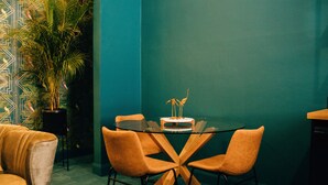 A room with a teal wall, a glass table with a central design, and orange chairs.