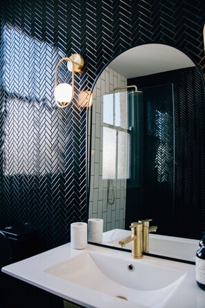 A bathroom with a white sink, gold faucets, and a mirror. - Rooms of Renown (Leeton)