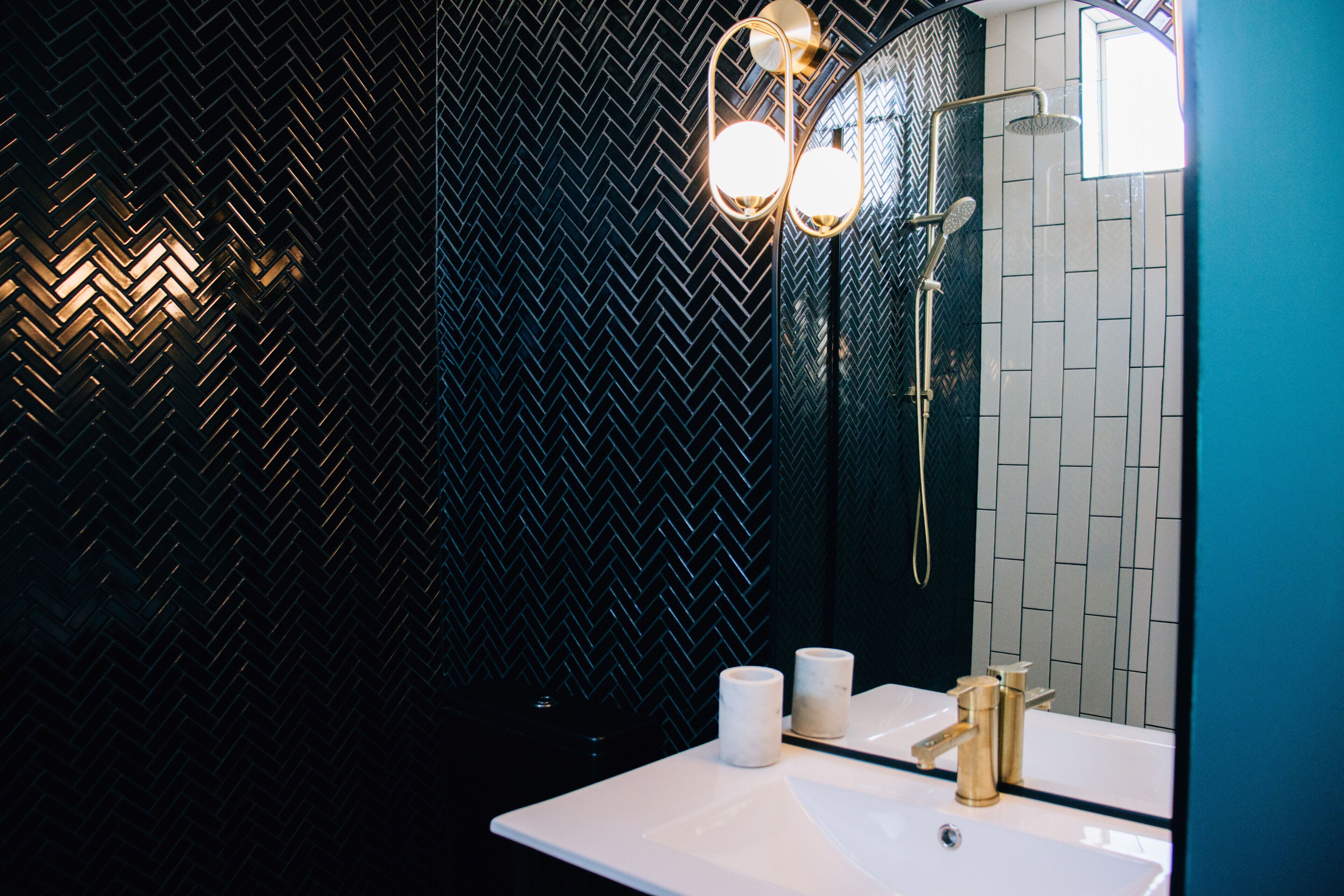 A bathroom with a herringbone-patterned wall, a white sink, a gold faucet, and a mirror with a gold frame.