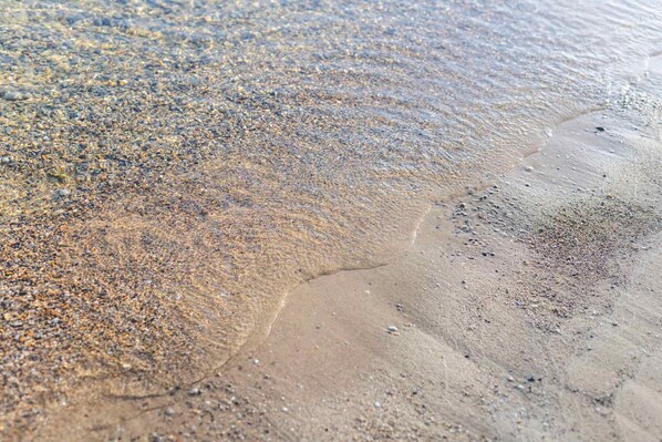 A close-up of a beach with clear water, pebbles, and sand.