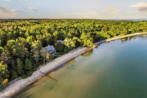 An aerial view of a lakeside property with dense forest, a sandy beach, and a small dock. - Paradesia Cove (Northport)
