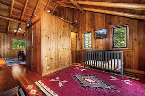 A wooden cabin interior with a crib, a rug, and a painting on the wall.