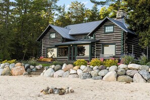 A log cabin with a stone chimney, a porch with a bench, and a stone wall in front. - Paradesia Cove (Northport)