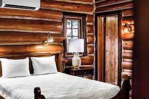A log cabin room with a bed, a window, a lamp, and a door.