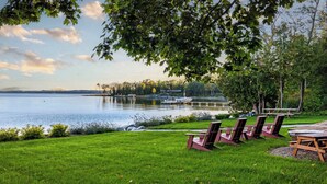 Une vue sur le lac, avec une zone herbeuse, des chaises longues et un quai où sont amarrés des bateaux.