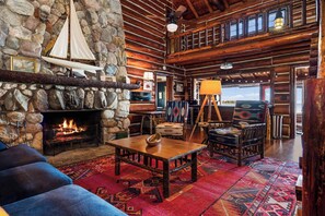A rustic interior with a stone fireplace, wooden furniture, and a view of the outdoors. - Paradesia Cove (Northport)