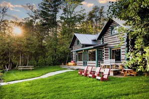 A log cabin with a porch, outdoor seating, and a pathway leading to the entrance. - Paradesia Cove (Northport)