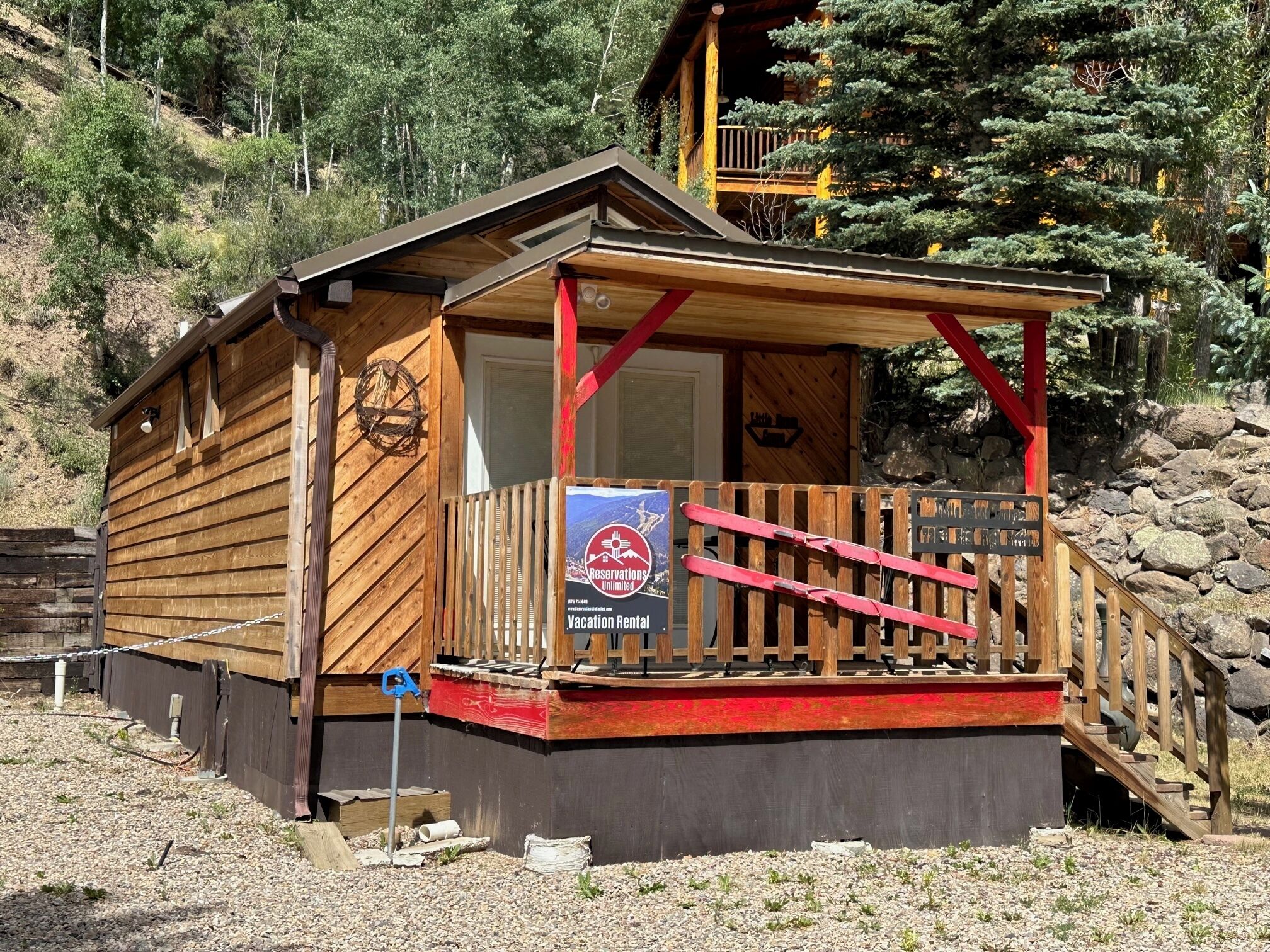 Eine Holzhütte mit Veranda, einem Schild mit der Aufschrift 'Reservations Unlimited Vacation Rental' und einer Holztreppe, die zu einer Terrasse führt.