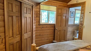 Ein Schlafzimmer einer Holzhütte mit Bett, Fenster und Tür.