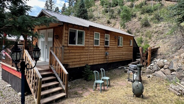 Eine Holzhütte mit einer Veranda, einer kleinen Terrasse und einem Patio mit Sitzgelegenheiten.