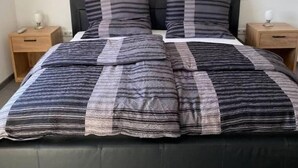 A bed with a striped blanket and two pillows, flanked by two bedside tables with lamps. - holiday flat "Felina" (Passau)