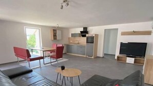 A modern living room with a black leather sofa, red cushions, a small round table, and a TV. - holiday flat "Felina" (Passau)