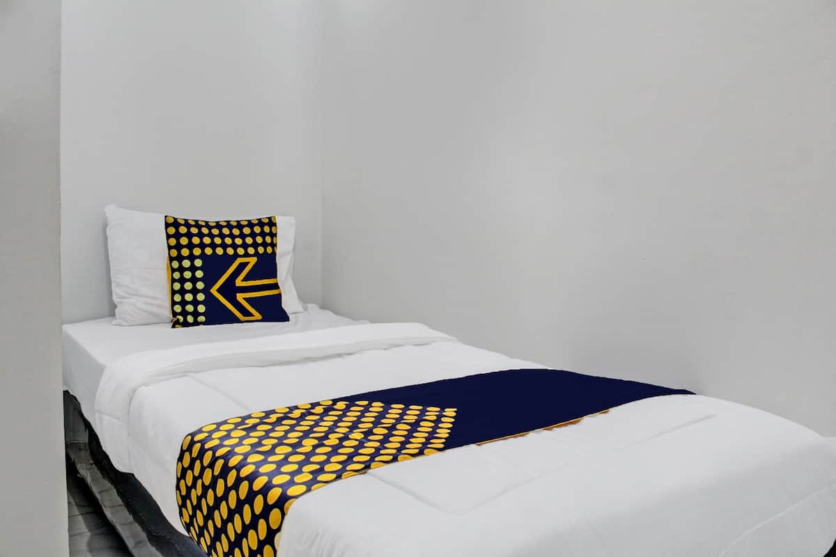 Un lit simple avec une literie blanche et un plaid à pois bleu marine et jaunes.