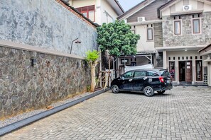 A black SUV parked on a cobblestone driveway in front of a building with a stone facade and a large tree. - OYO Life 92509 Maulana Guest House Simpur (Bandar Lampung)