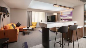 Een moderne hotelkamer met een zithoek, een eethoek en een grote televisie.