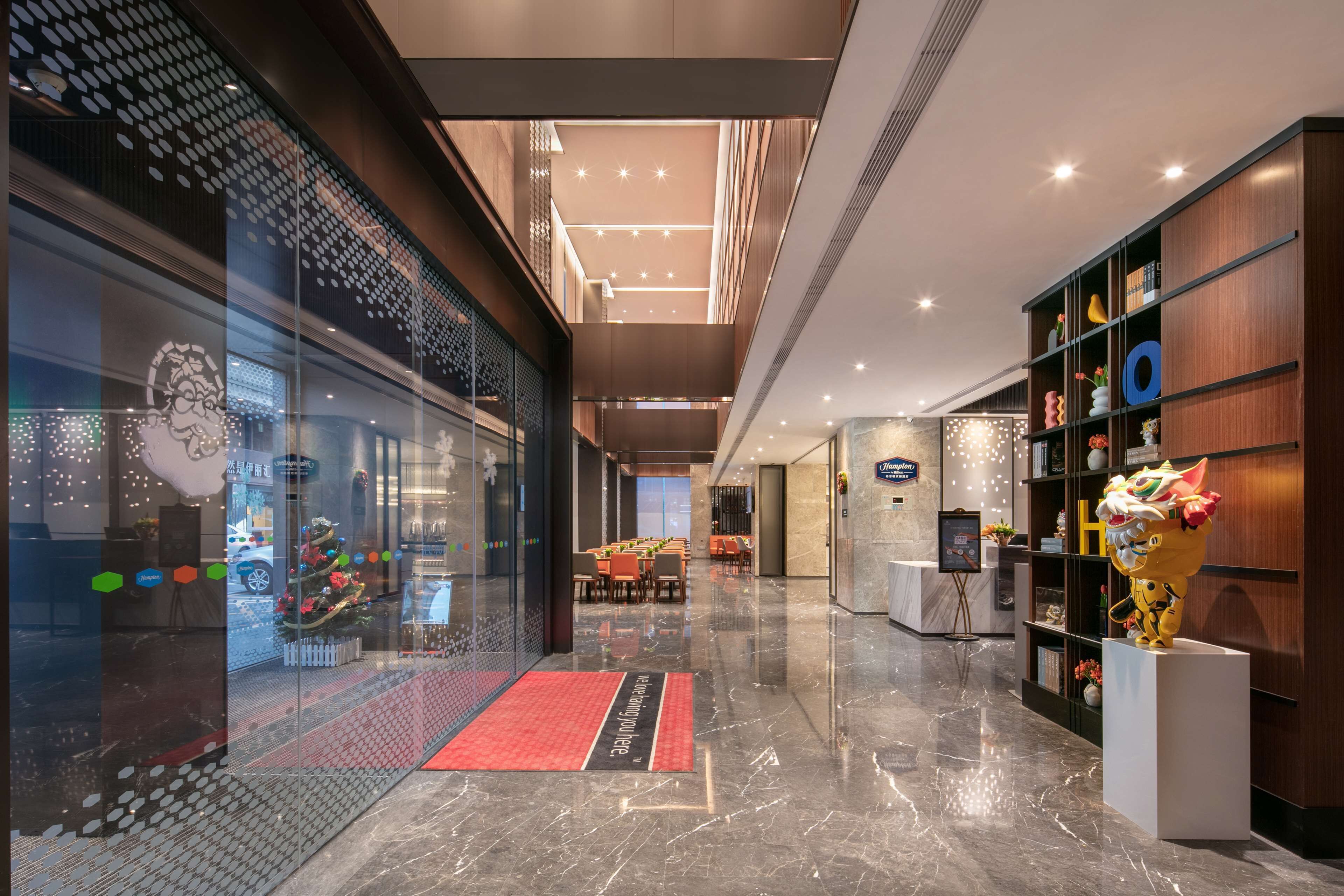 Un moderno vestíbulo de hotel con una pared de vidrio, una alfombra roja y una estatua de tigre.