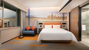 Een moderne hotelkamer met een groot bed, een blauwe fauteuil en een stadsgezicht muurschildering.