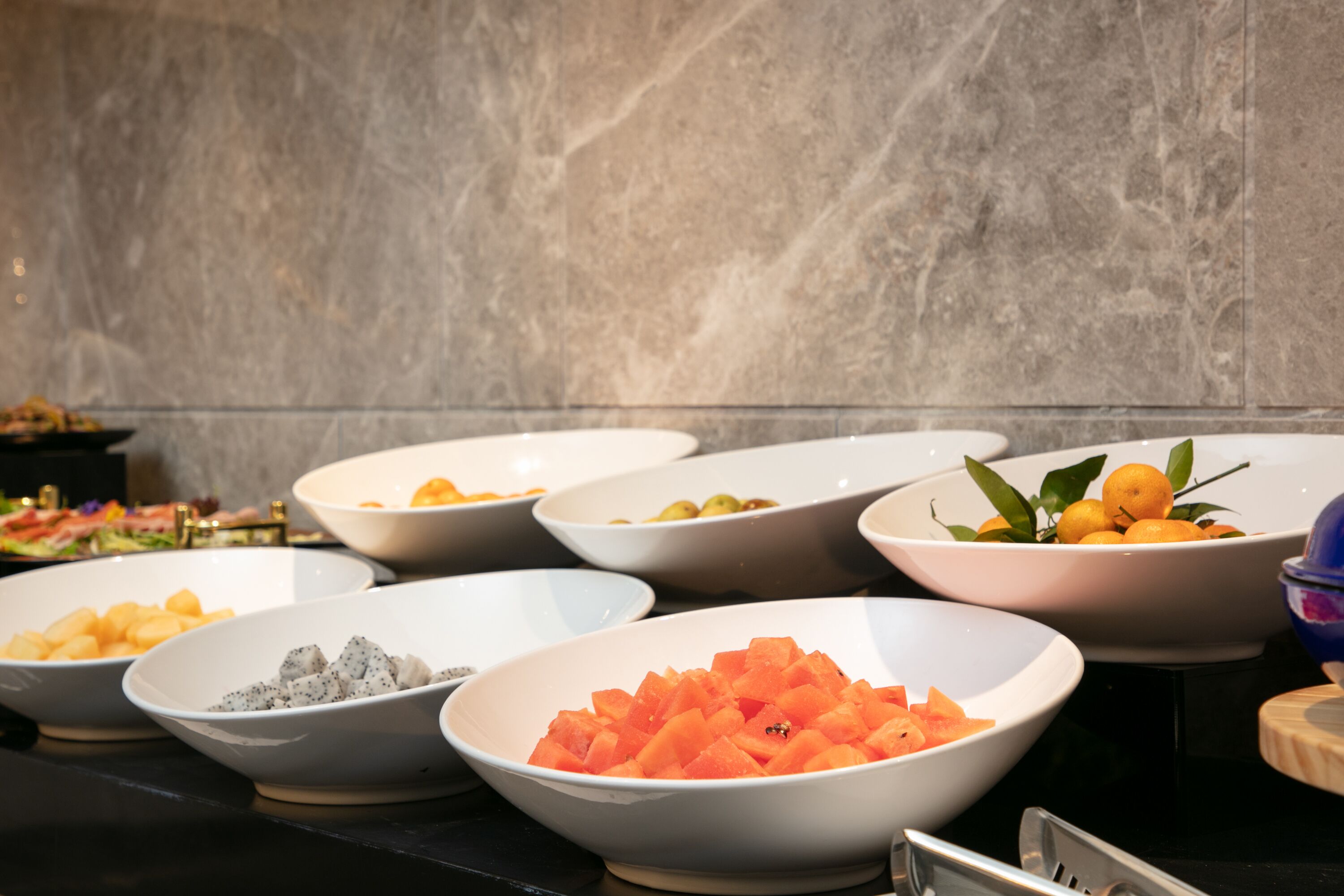 A buffet table with various bowls of food, including fruits and vegetables.