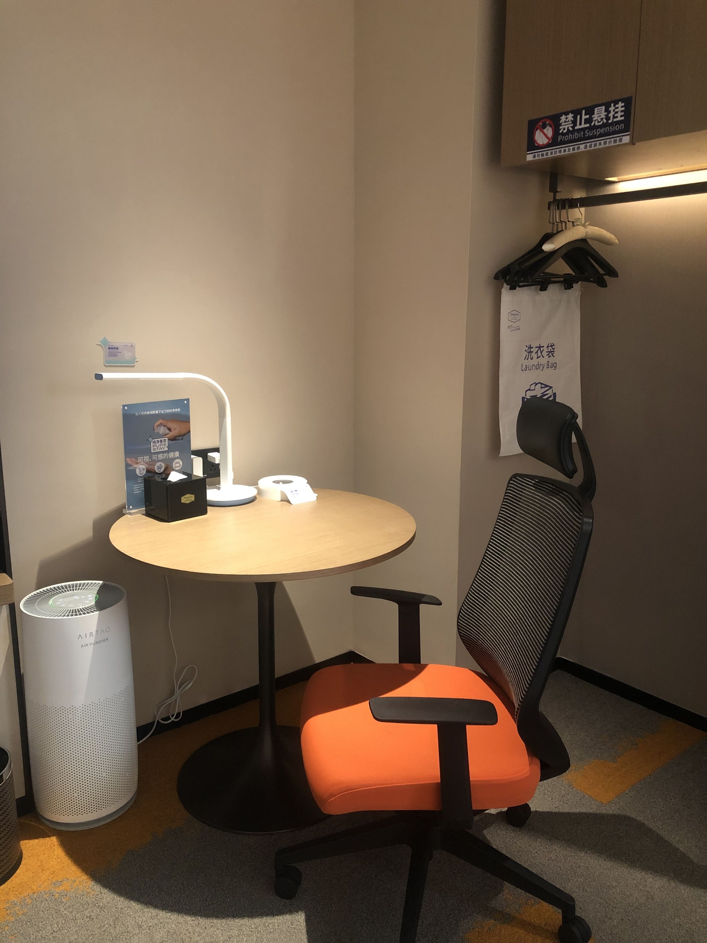 Un petit bureau comprenant une table ronde, une chaise, un purificateur d’air, une poubelle et un panneau indiquant qu’il est interdit d’y accrocher des objets.
