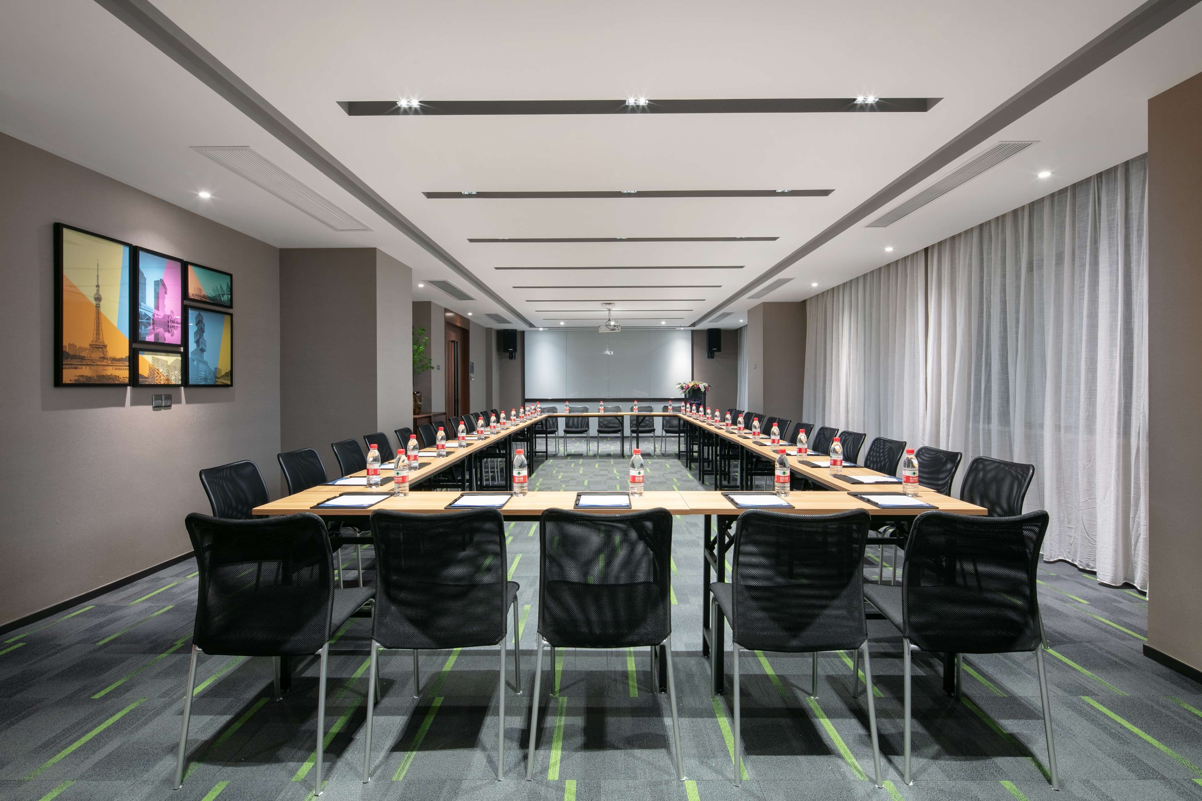 A conference room with a long table, black chairs, and a projector screen.