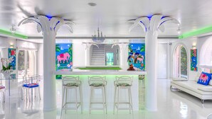 Una cocina moderna con una isla central, taburetes de bar blancos y un sofá blanco con un cojín colorido.