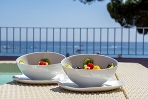 Two white bowls of fruit on a table with a view of the sea and a fence in the background. - The Pink Elephant Hotel (Sant Feliu de Guixols)