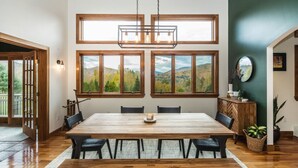 A dining area with a large wooden table, multiple chairs, and a view of a mountainous landscape through large windows.