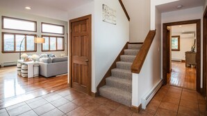 A spacious living room with a large window, a wooden door, and a staircase leading to another room.