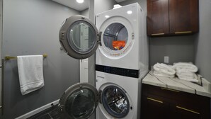 Un espace buanderie avec deux machines à laver superposées, une serviette blanche suspendue à un étendoir et un comptoir en marbre sur lequel sont pliées des serviettes.