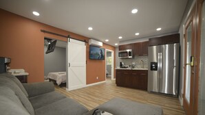 Un salon moderne avec un canapé gris, un plaid à motifs et un coin cuisine comprenant un réfrigérateur en acier inoxydable, un four à micro-ondes et des meubles de rangement en bois.