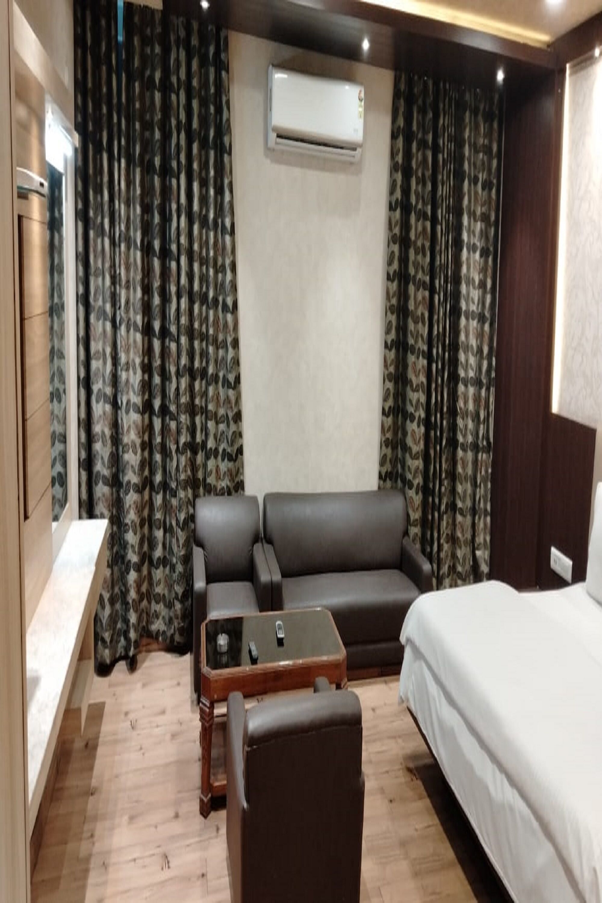 A hotel room with a sofa, a small table, a bed, and an air conditioning unit.