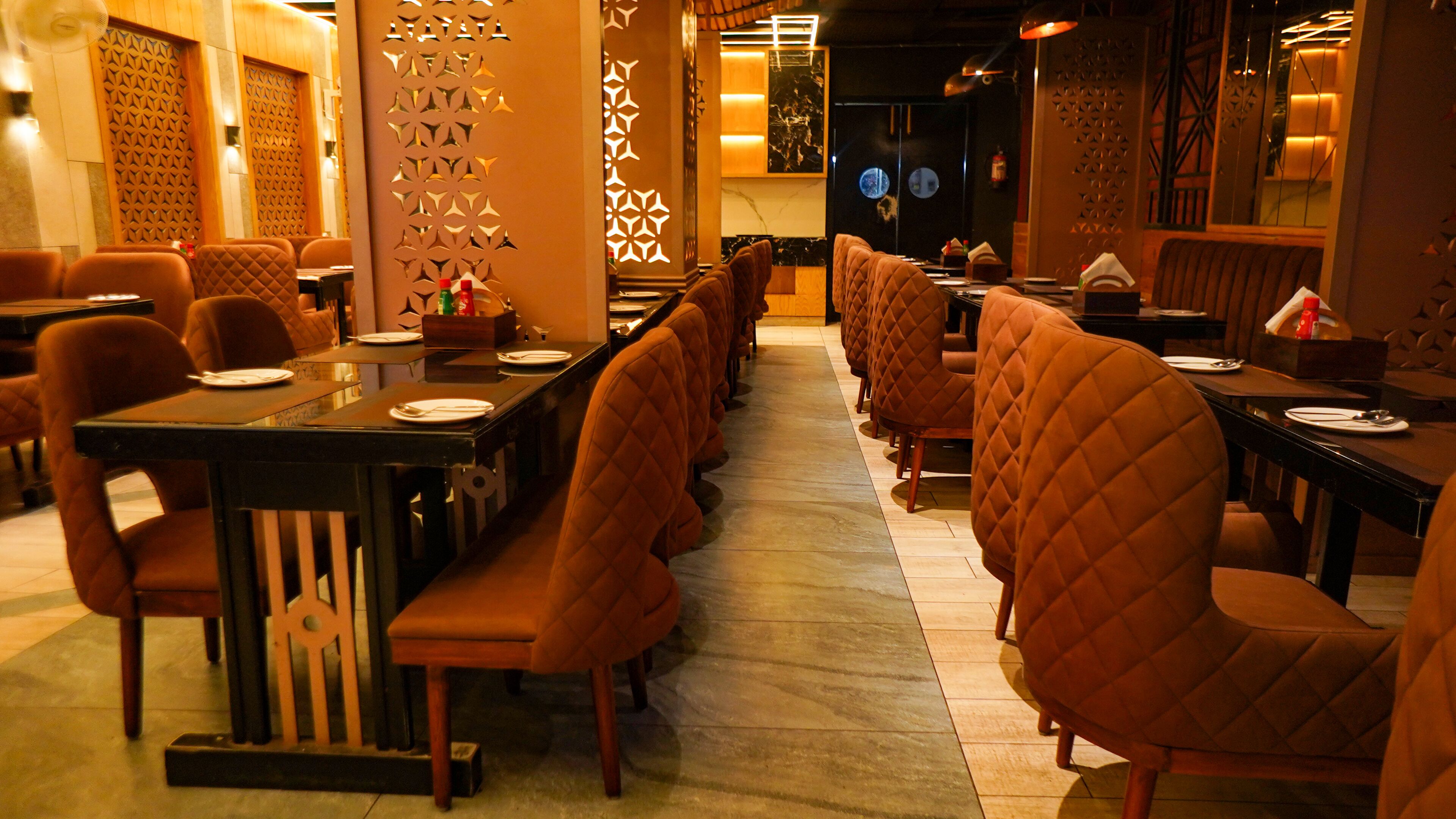 A restaurant with long communal tables and cushioned booths, featuring a patterned wall and warm lighting.
