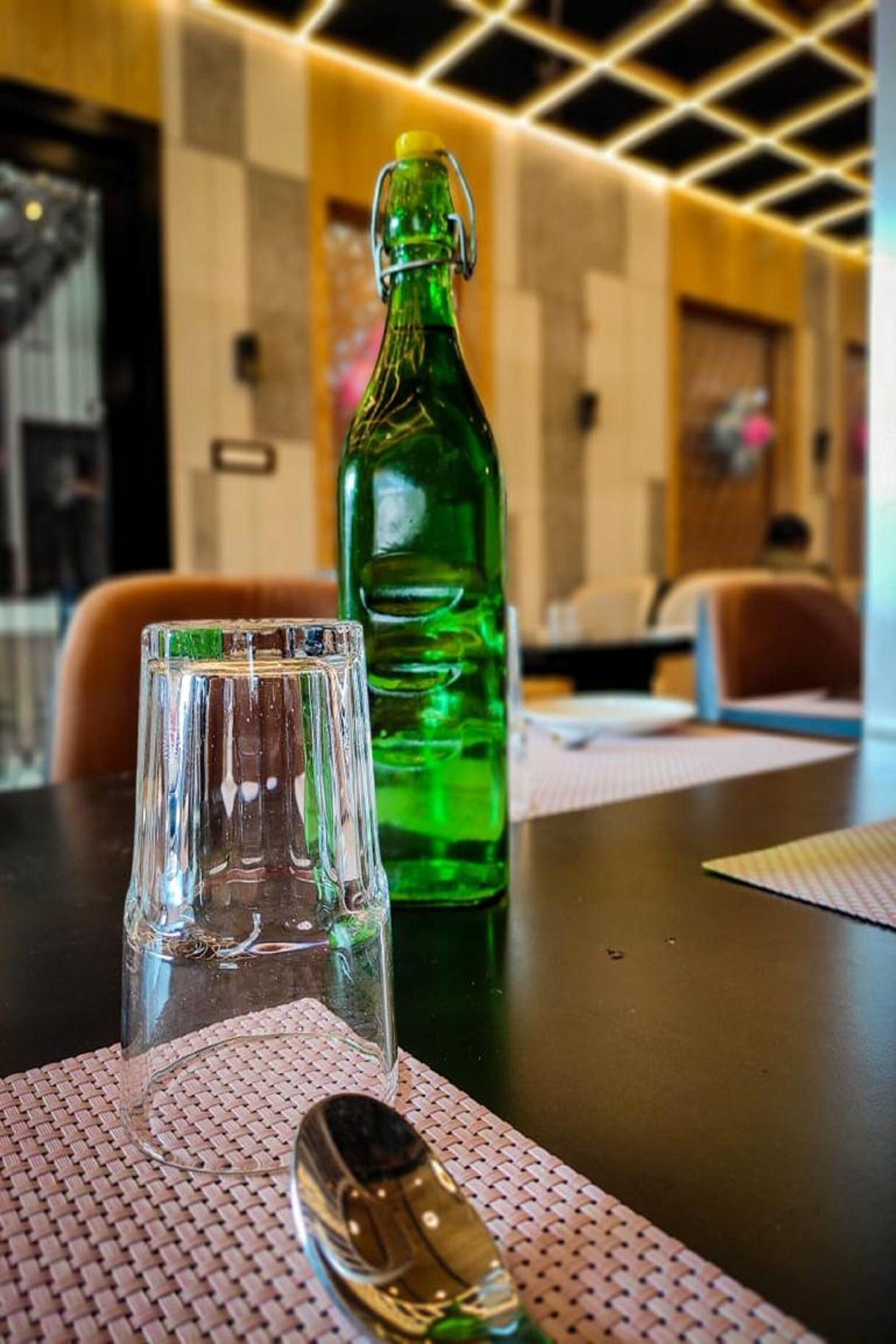 A table with a clear glass, a green bottle, and a spoon.