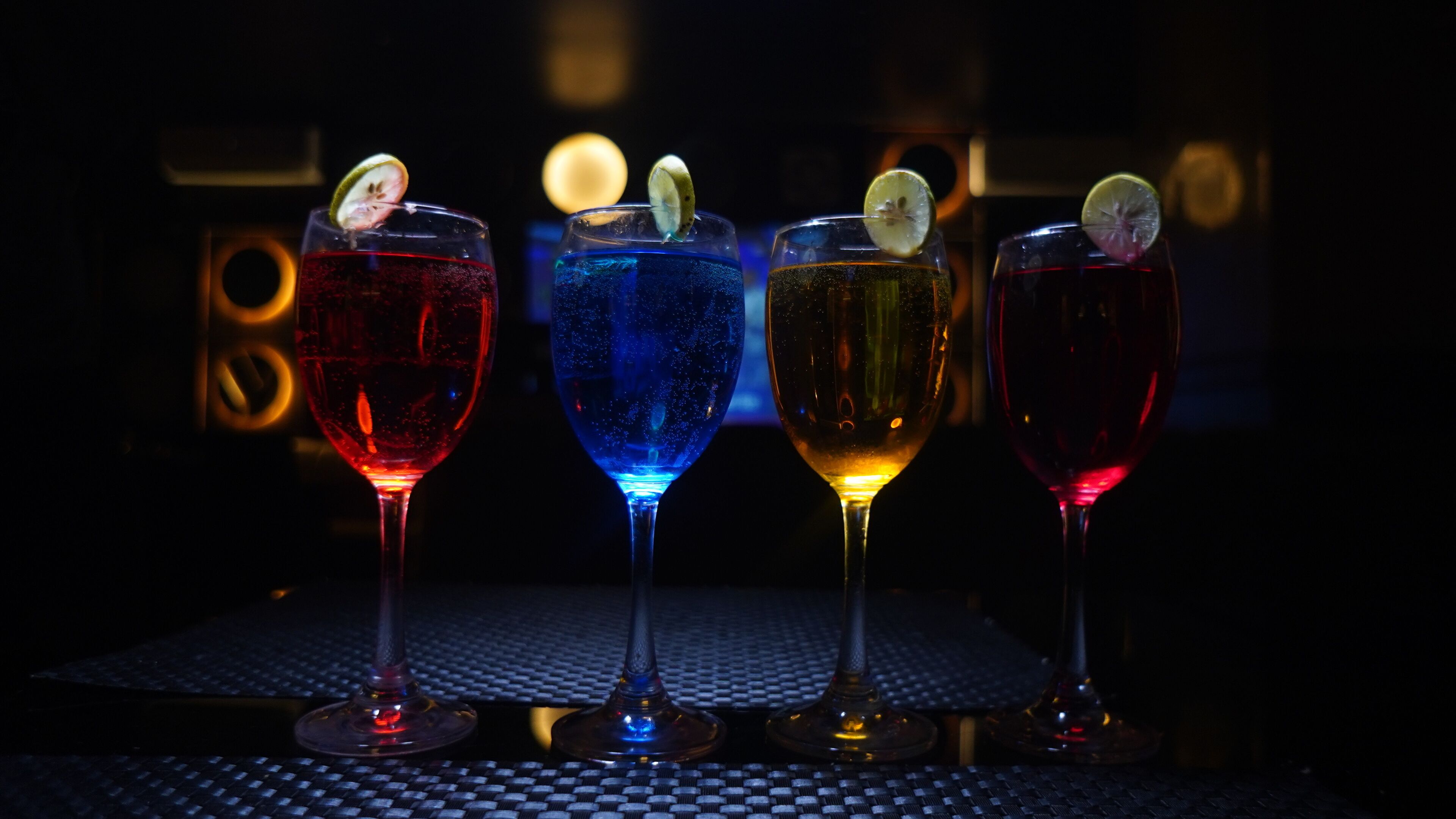 Four glasses of different colored beverages on a table with a checkered pattern.