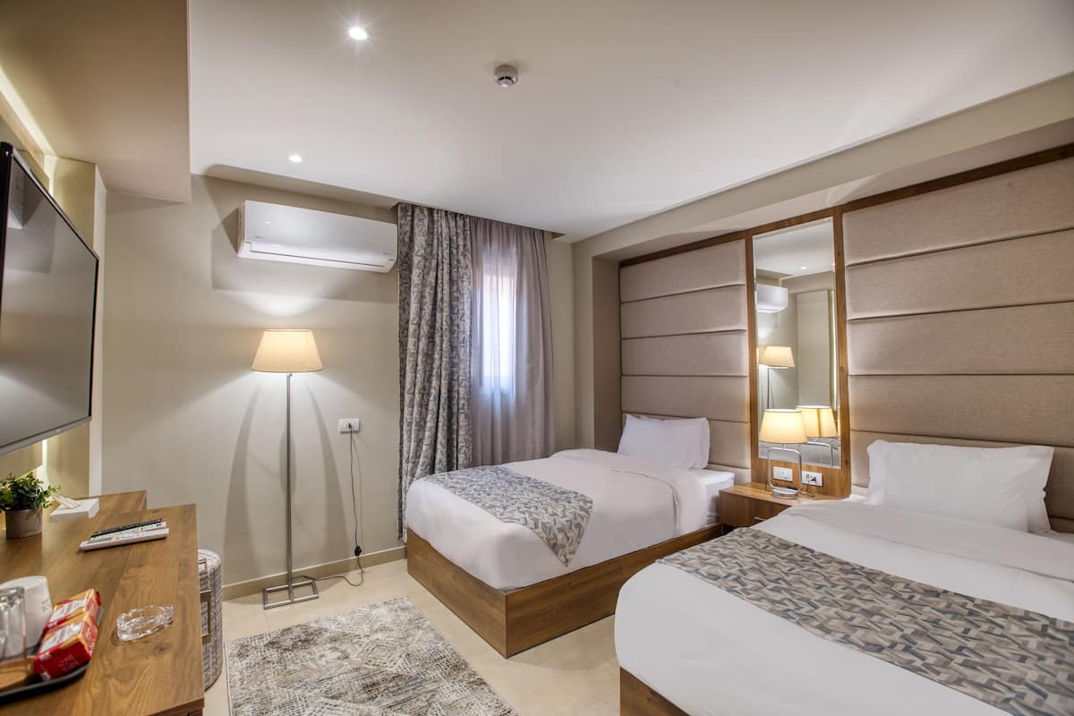 A hotel room with two beds, a flat-screen TV, a desk with a lamp, and a large mirror.
