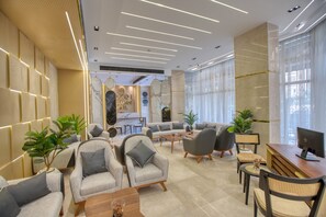 A modern hotel lobby with sofas, armchairs, a reception desk, and large windows.