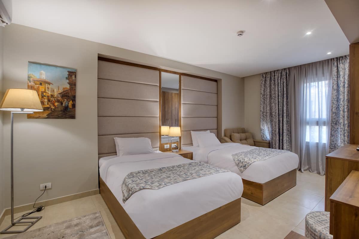 A hotel room with two beds, a desk, a chair, and a painting on the wall.